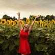 Woman in a red dress throwing a hat in a sunflower field with a blue sky.